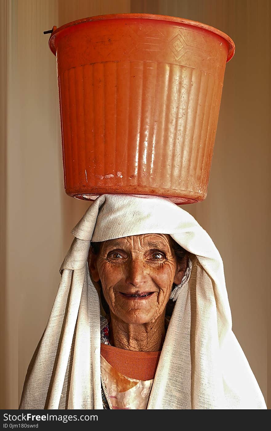 Portrait Photo of Woman Carrying Orange Plastic Pail on Head