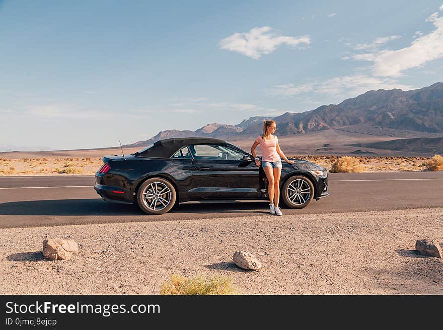 Young girl standing by the black Ford Mustang GT convertible at the side of the road. Nevada, USA.