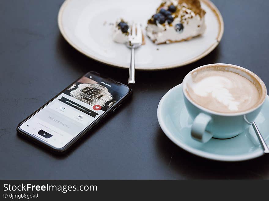 Black Smartphone Beside Coffee Mug in Shallow Focus Lens