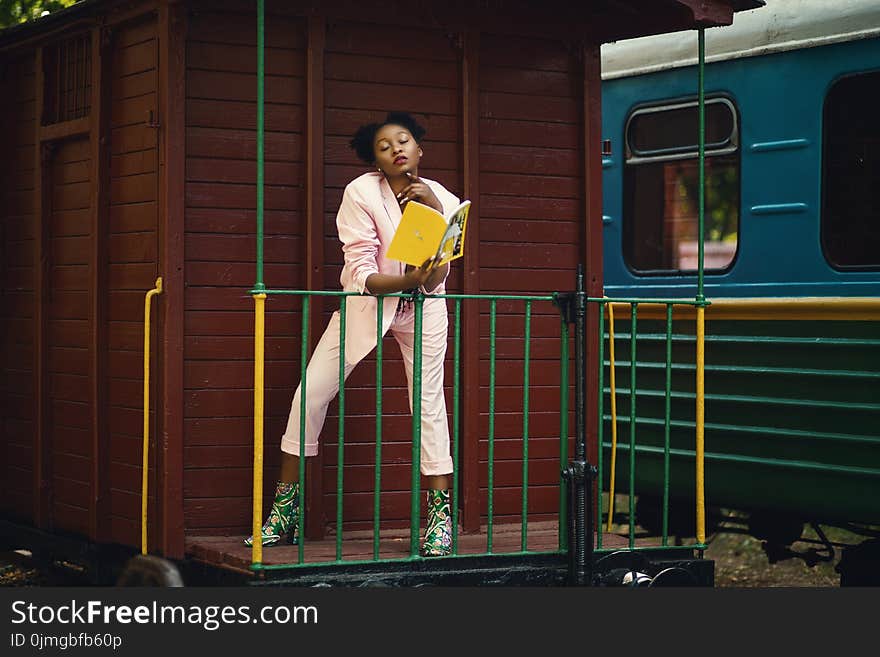 Woman Wearing Pink Blazer, Pants and Green Heeled Shoes Holding Yellow Covered Book