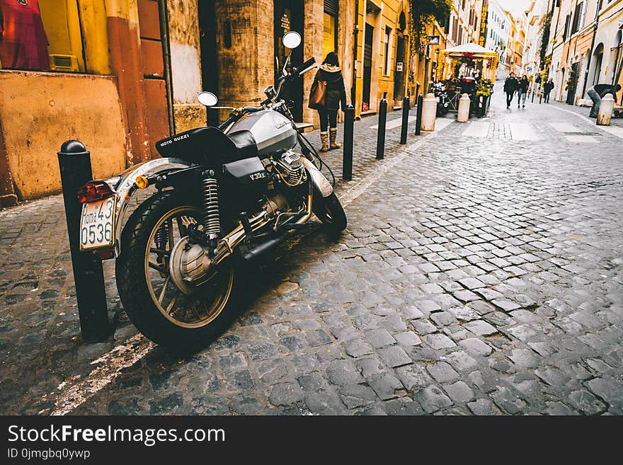 Photograph of Motorcycle Parked Beside Park Bars Near Woman Walking Through Street