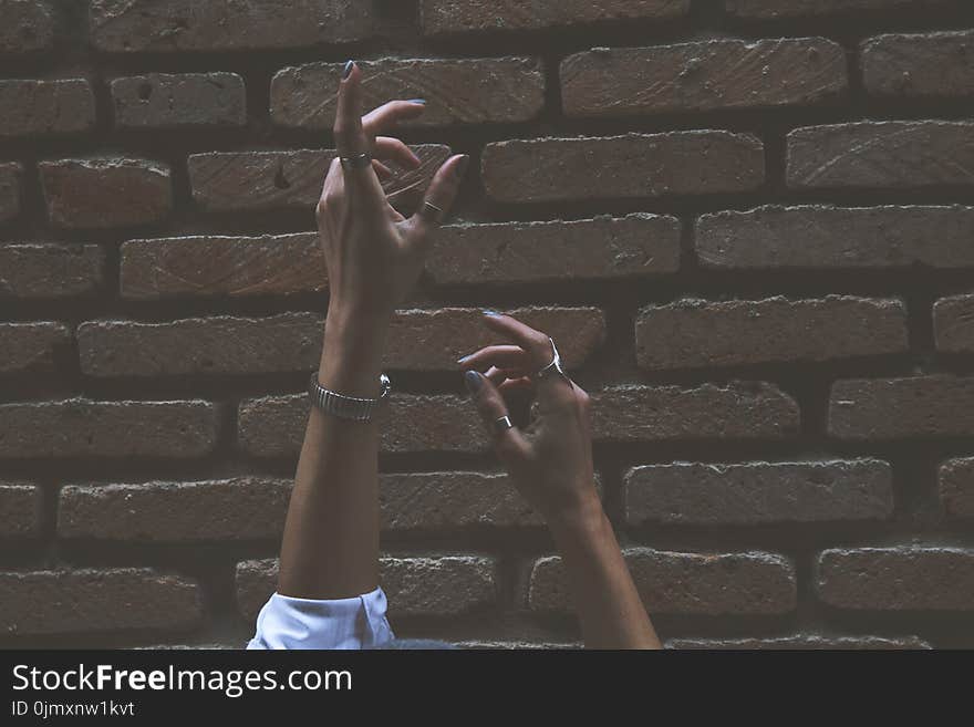 Person Raising Its Two Hand Beside Brown Brick Wall