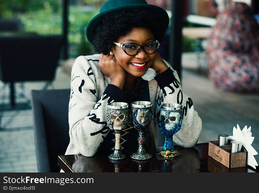 Depth of Field Photography of Woman Leaning Elbow on Table With Three Skull Printed Goblets