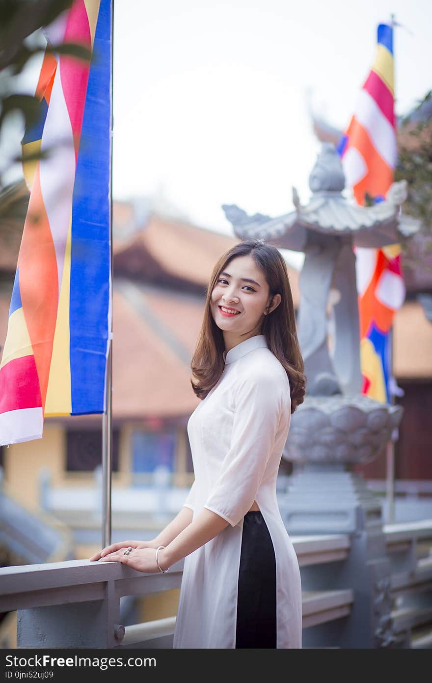 Depth of Field Photo of Woman Wearing White Dress Standing Near Flag Pole