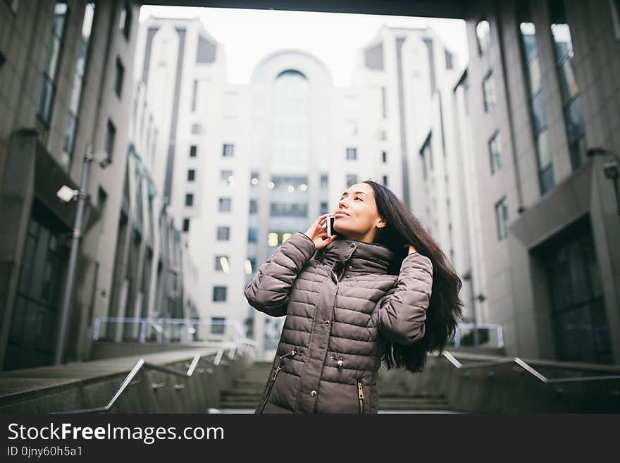 Young girl talking on mobile phone in courtyard business center. girl with long dark hair dressed in winter jacket in cold weather