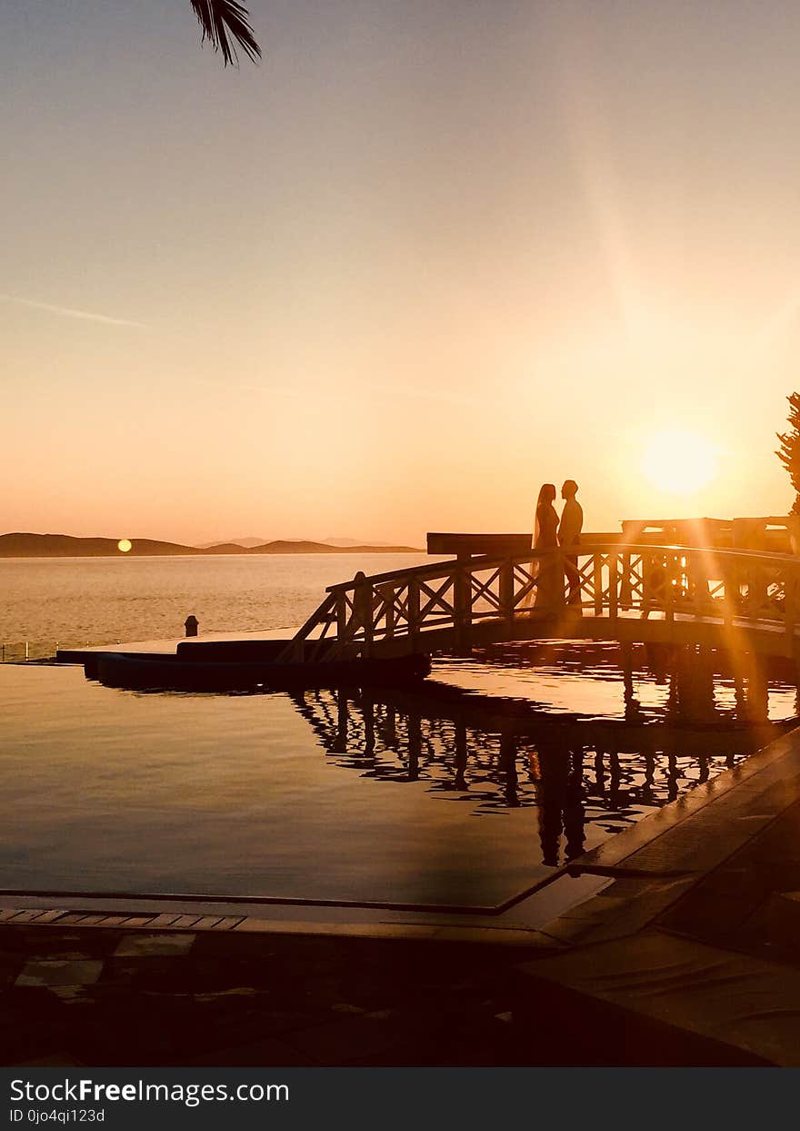 Silhouette of Couple Standing Near Sea Dock at Golden Hour