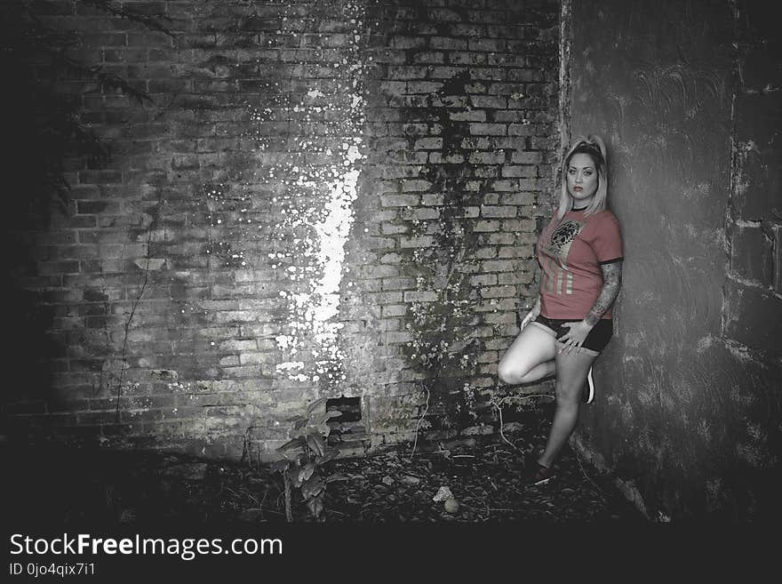 Woman Wearing Orange Crew-neck Short-sleeved Shirt Leaning on Concrete Wall