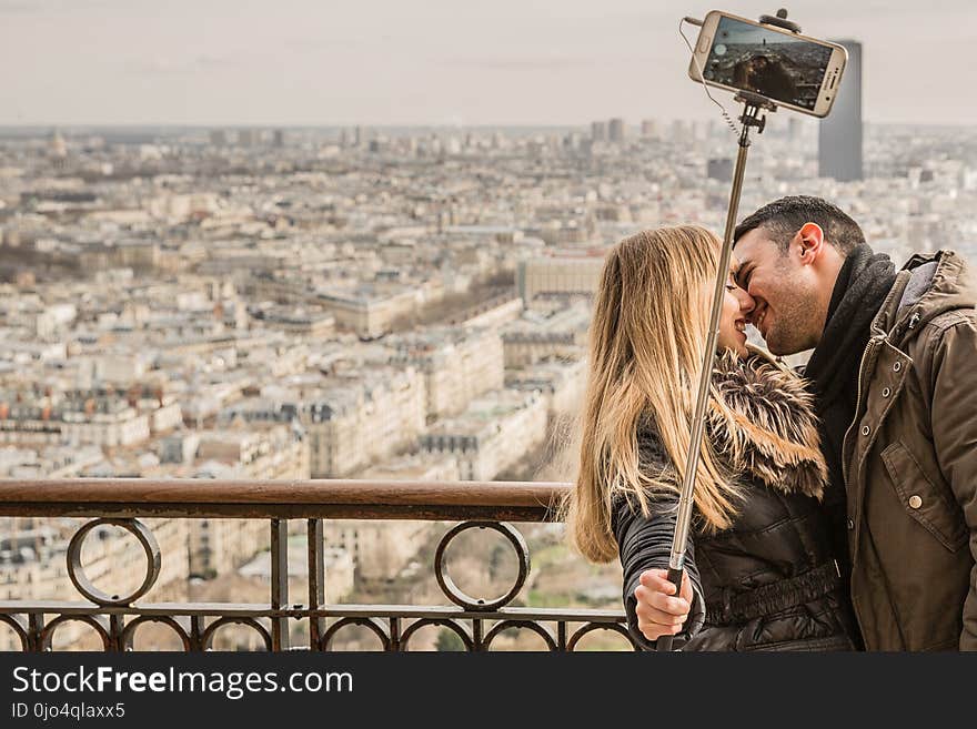 Man Kissing Woman Holding Selfie Stick