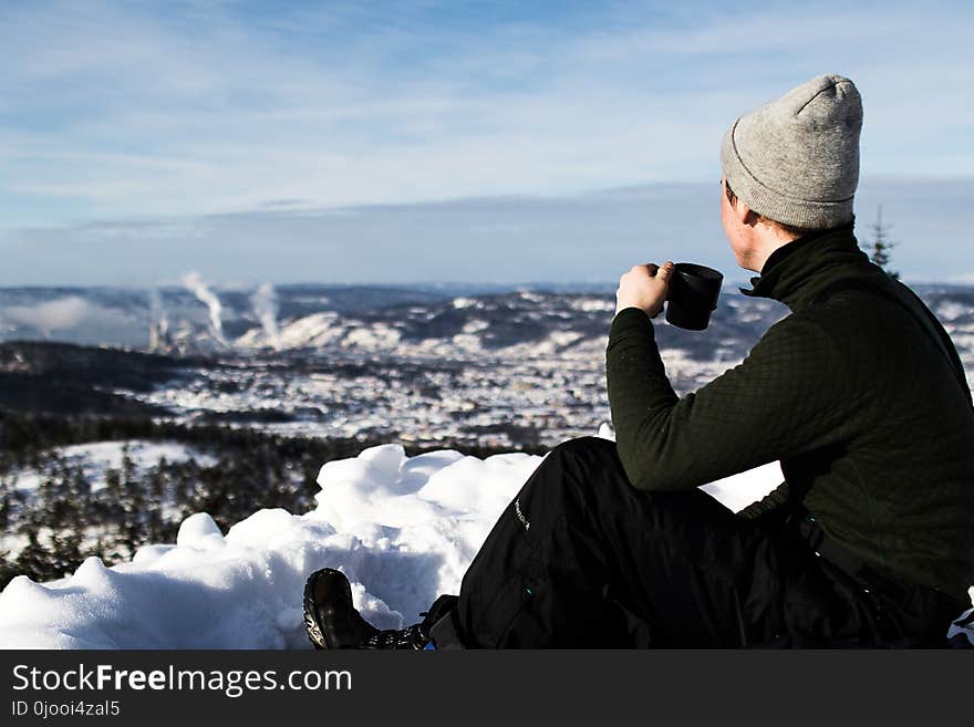 Man Wearing Jacket and Holding Cup Sitting on the Snow