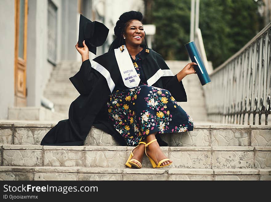 Photo of Woman Wearing Academic Dress and Floral Dress Sitting on Stairway