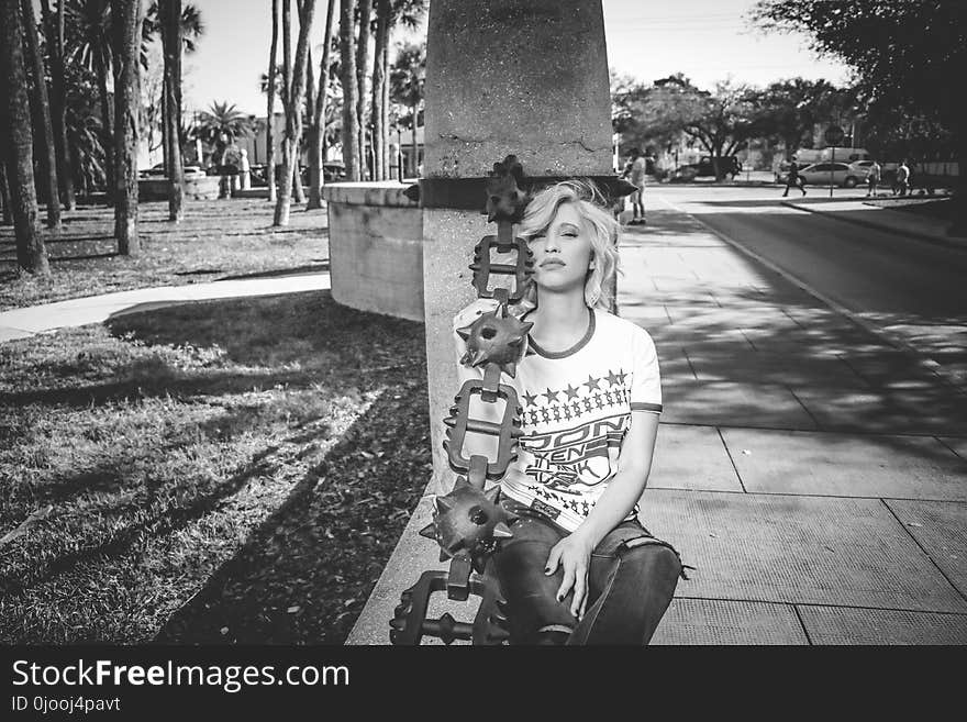 Grayscale Photo of Woman Leaning on Concrete Post