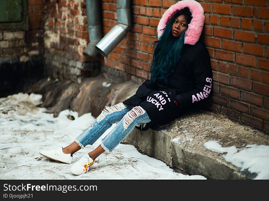 Woman Wearing Black and Pink Parka Leaning on Brown Brick Wall