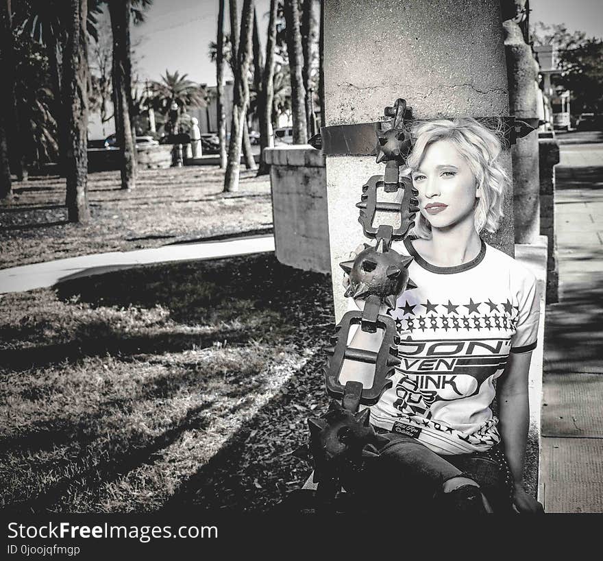 Woman Sitting Beside Gray Concrete Post Grayscale Photo