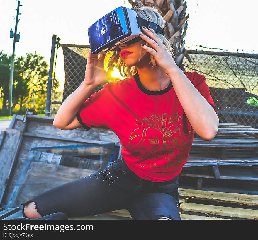 Woman Wearing Red and Black Top and Blue Distressed Bottoms Wearing Gray and Black Virtual Reality Sunglasses