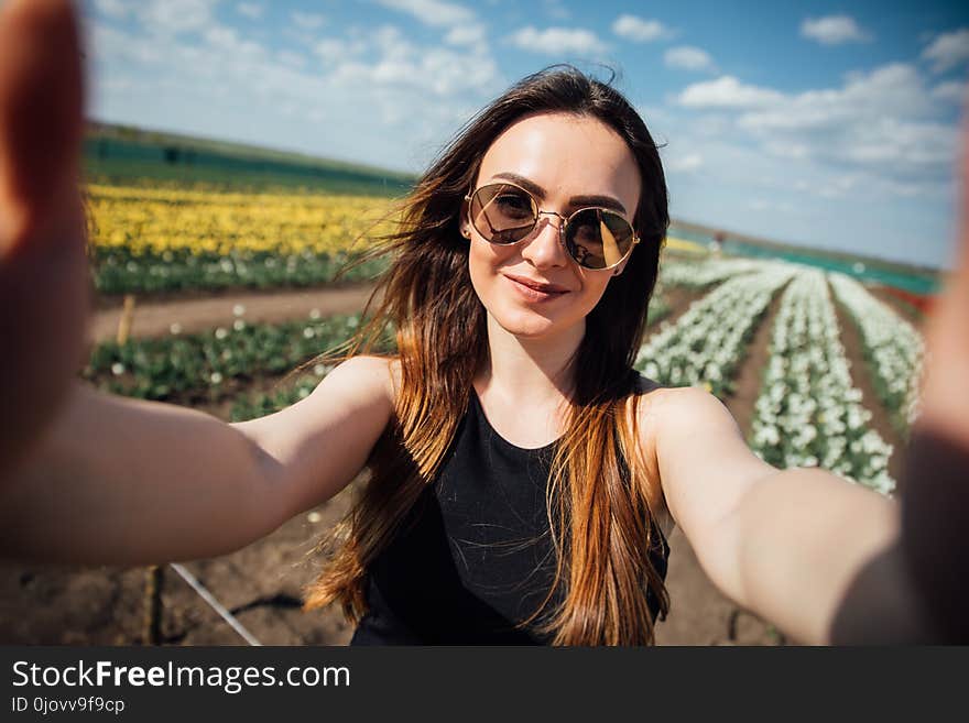 Young beautiful woman wear sunglasses make selfie in tulips flower field in sunny spring day