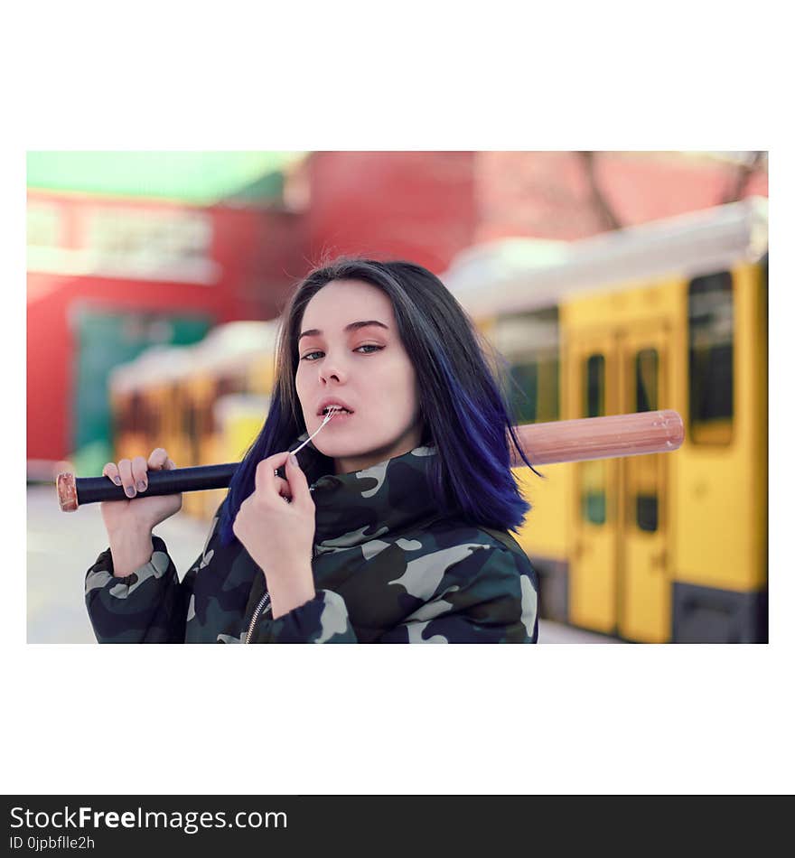 Woman Wearing Green and Beige Camouflage Jacket While Holding Black and Brown Baseball Bat