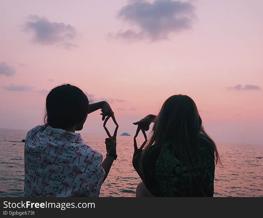 Two Woman Sitting in Front of Body of Water