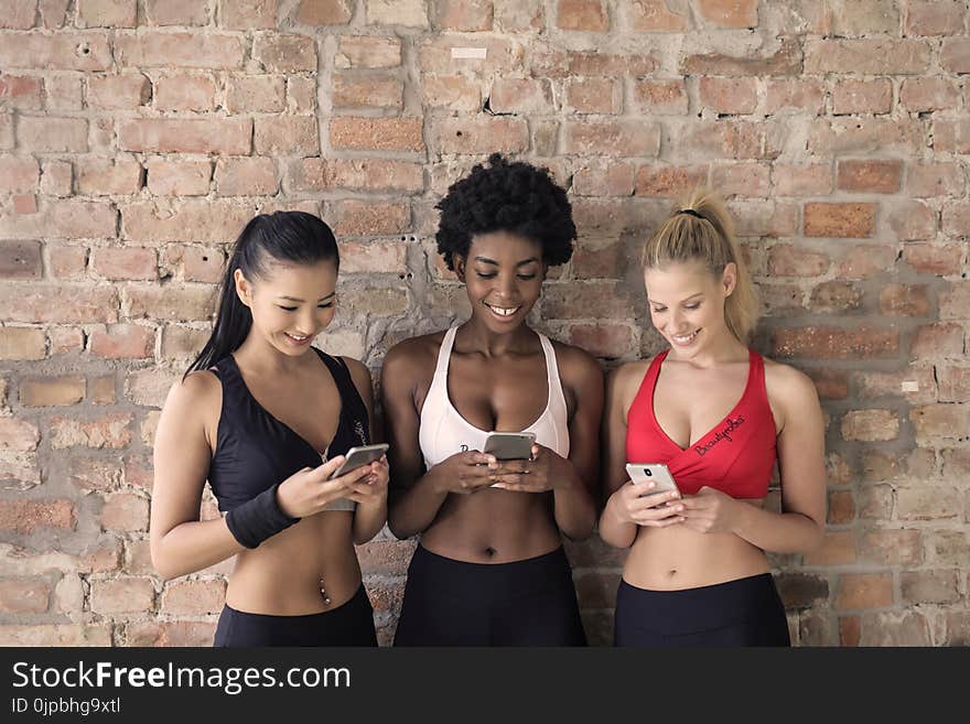 Three Woman in Assorted-color Sport Bras Holding and Watching Their Smartphones