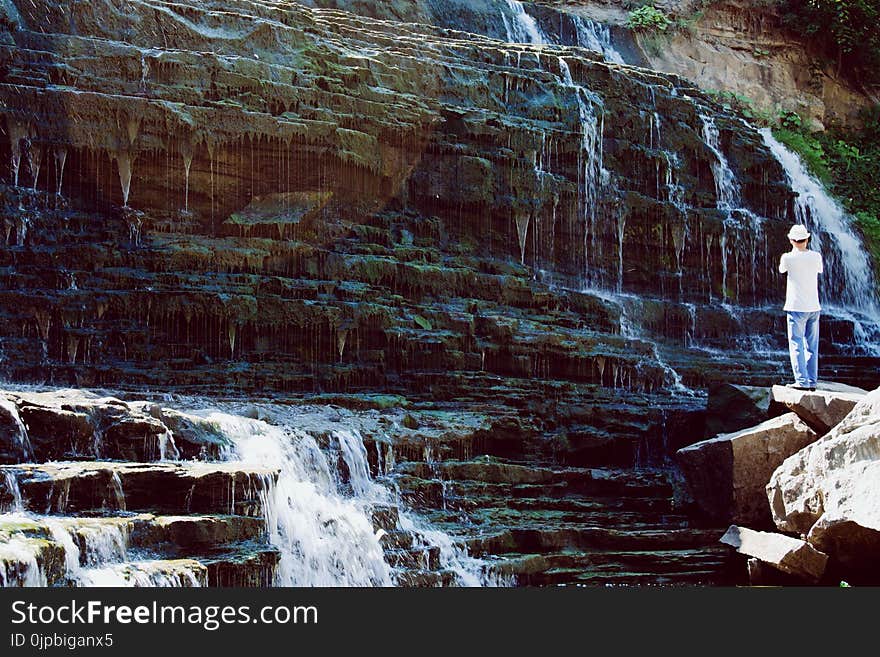 Man in White T-shirt and Blue Jeans Standing Near Water Falls