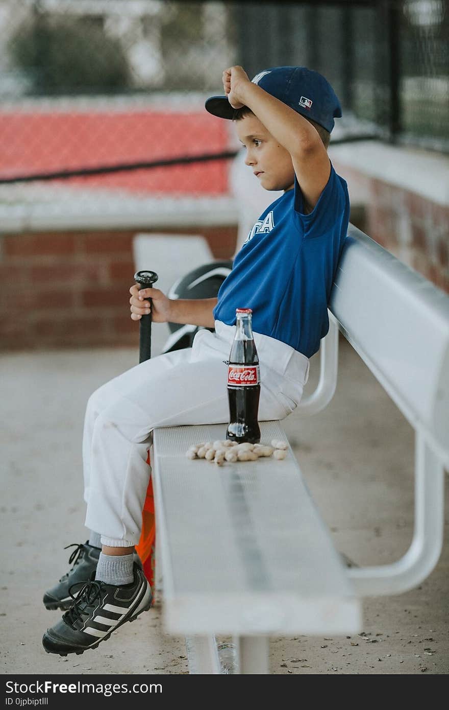 Selective Focus Photo of a Boy Wearing Baseball Gear Sitting on Bench Beside Coca-cola Bottle