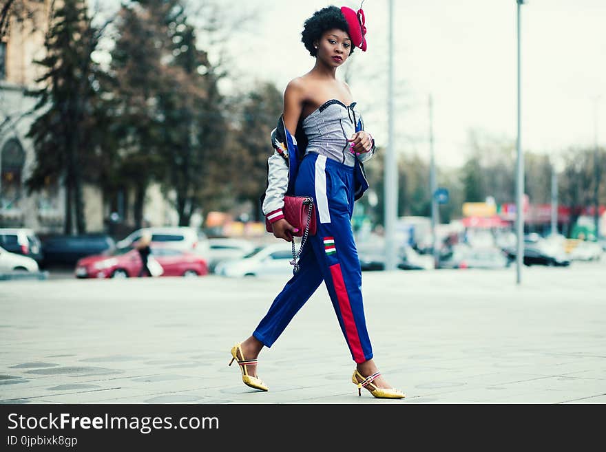 Woman Wearing White Sweetheart Neckline Shirt With Blue and Red Pants Walking Across the Street