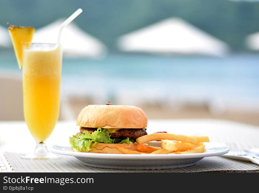 Burger With Lettuce and Fries on Plate Beside Pineapple Juice