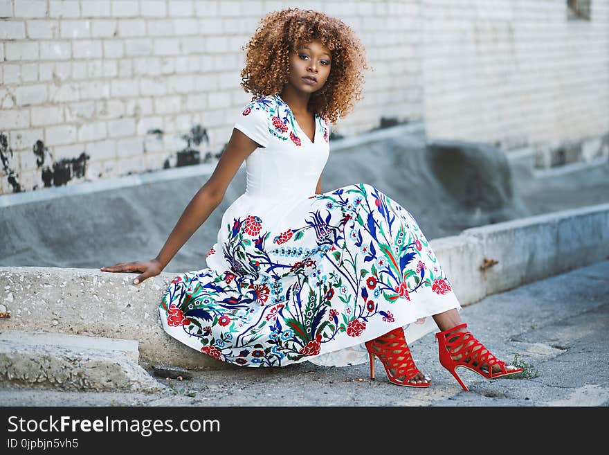 Woman in White and Multicolored Floral Flare Dress Sitting on Concrete