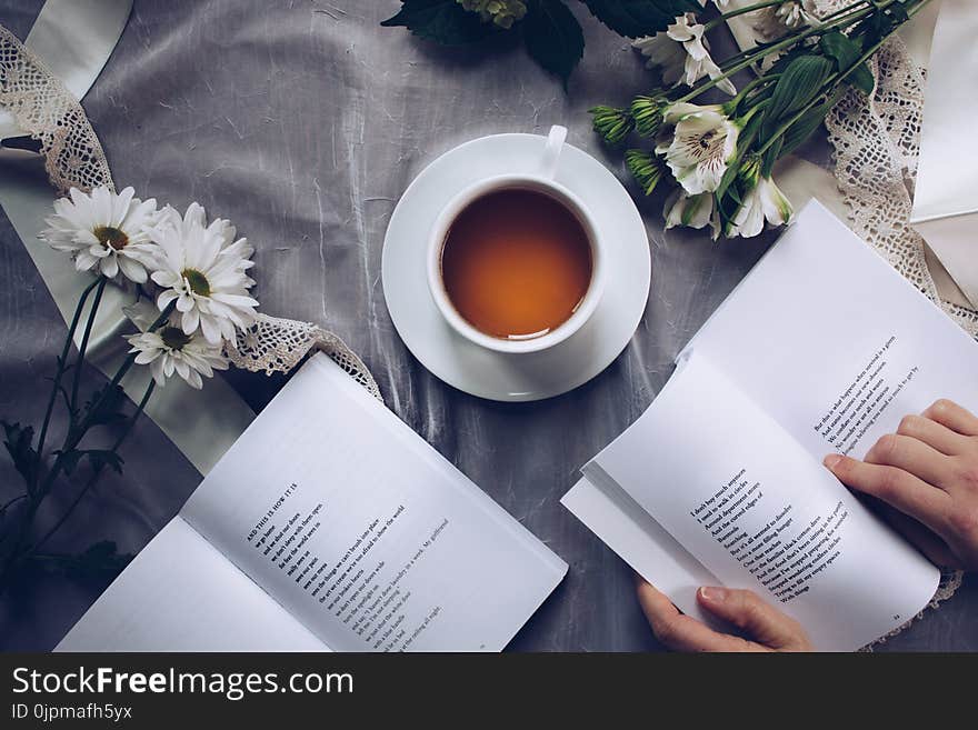 White Ceramic Teacup With Saucer Near Two Books Above Gray Floral Textile