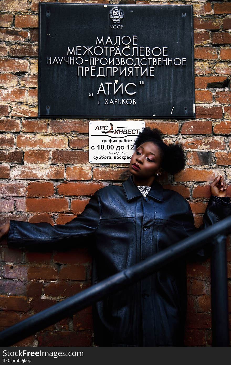 Woman in Black Leather Coat Leaning on Brick Wall