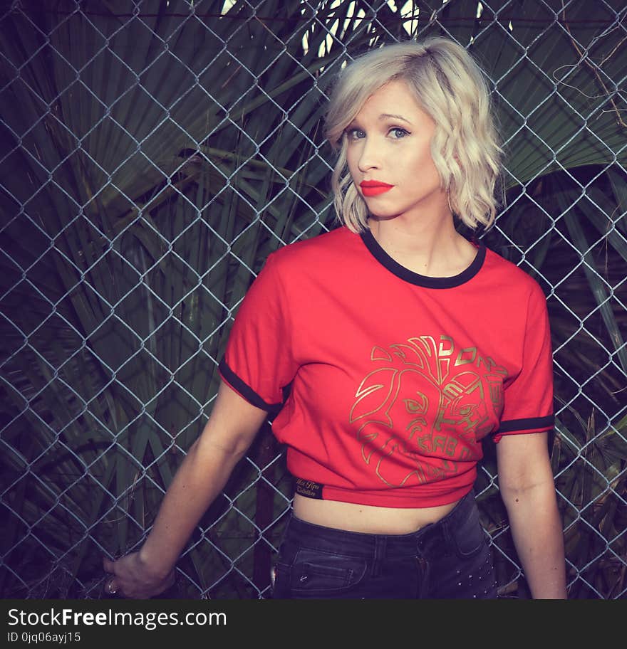 Woman in Red and Black T-shirt Standing Near Chain Fence