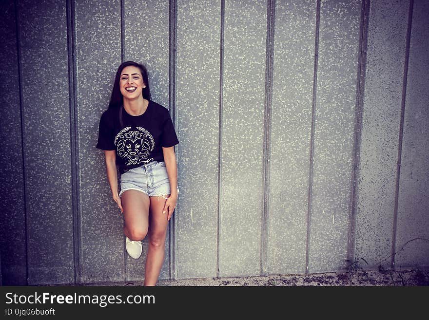 Woman Wearing Black and White Crew-neck T-shirt and Gray Denim Short Shorts Outfit Leaning on Gray Wall