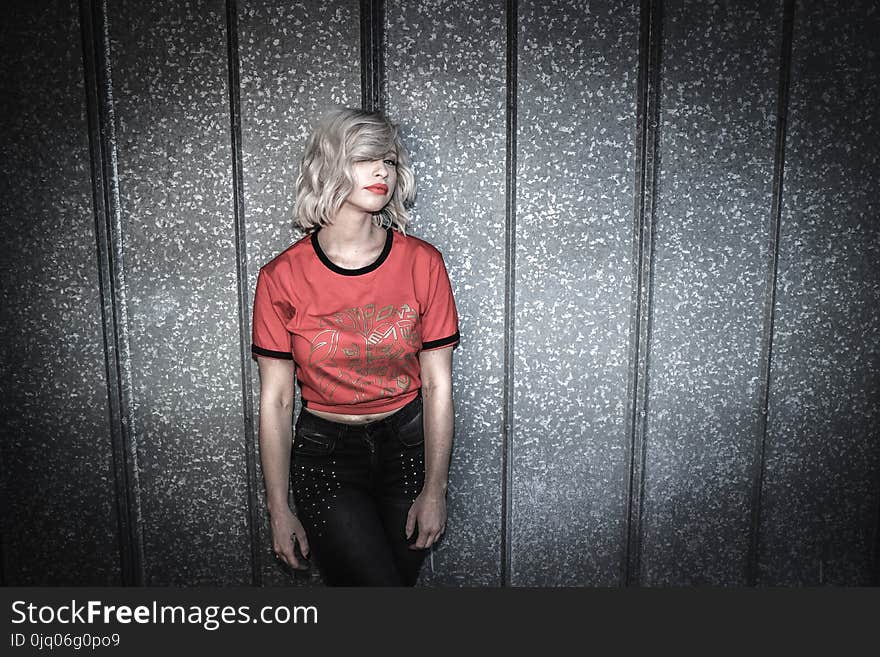 Woman Wearing Red and Black Scoop-neck Shirt and Black Bottoms Leaning on Gray Wall