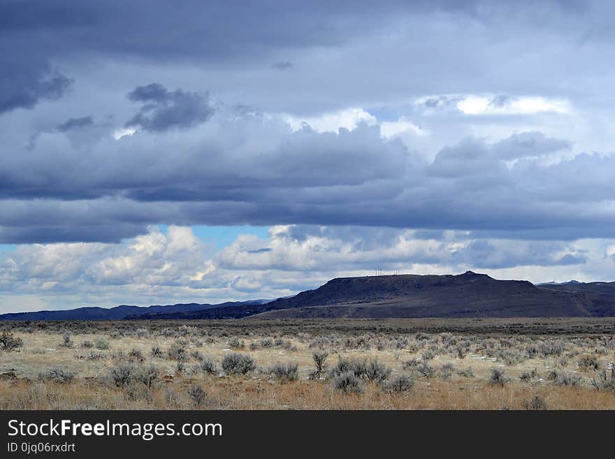 Gray Grass Field Leading to Mountains Under Gray Heavy Clouds