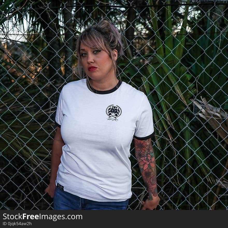 Female Wearing Black and White Crew-neck T-shirt and Blue Denim Bottoms Leaning on Chicken Wire