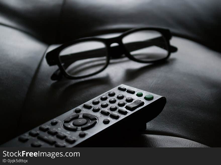 Grayscale Photo of Remote Control Near Eyeglasses