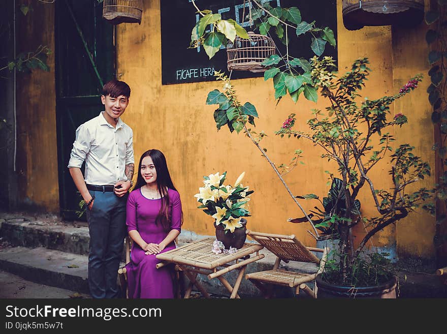 Sitting Woman Wearing Purple Elbow-sleeved Dress and Standing Man Wearing White Dress Shirt