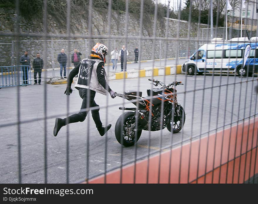 Man Holding Orange and Black Sports Bike on Asphalt Road