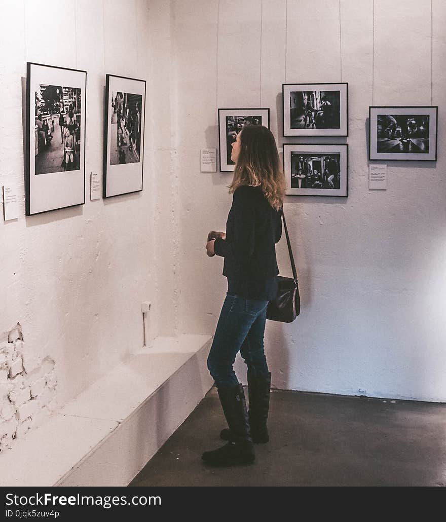 Woman Wearing Black Sweater and Blue Denim Jeans Staring at Paintings Inside Well-lit Room