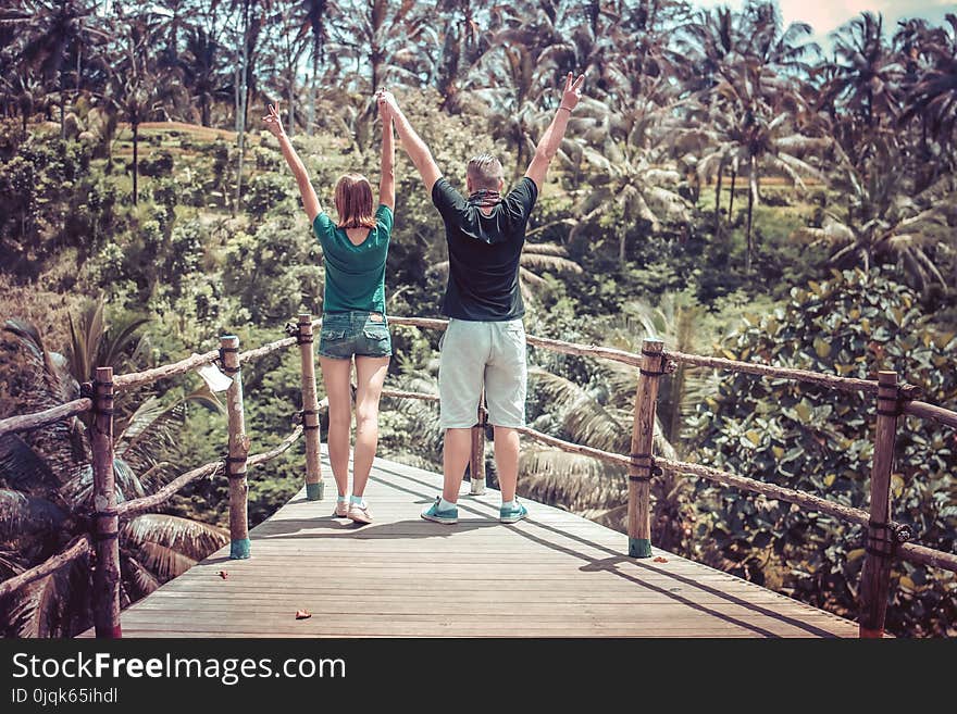 Man Wearing Black Shirt Beside a Woman in Green Shirt Raising Their Hands in the Air