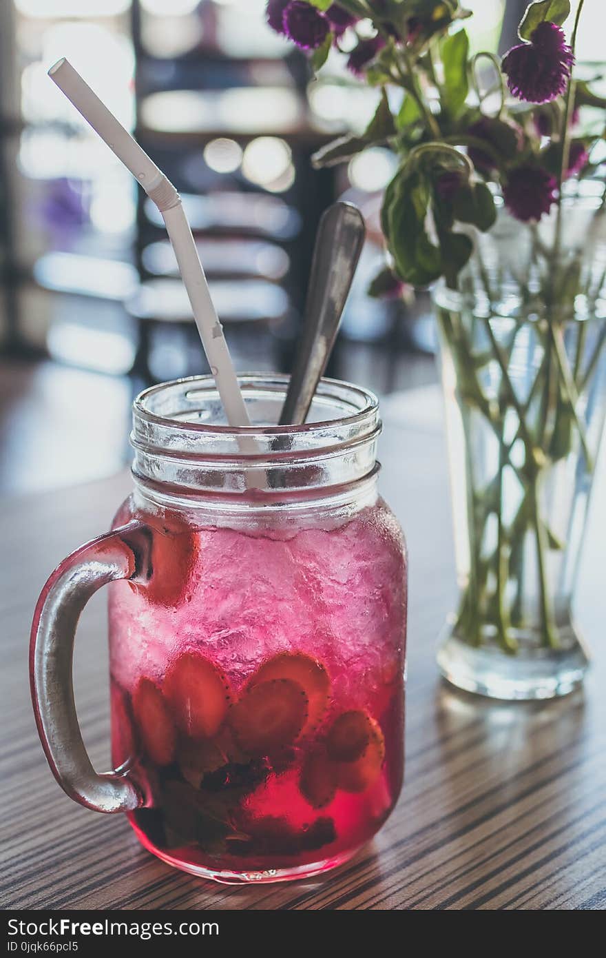 Red Beverage-filled Clear Glass Mason Mug With Straw Beside Purple Flowers in Vase