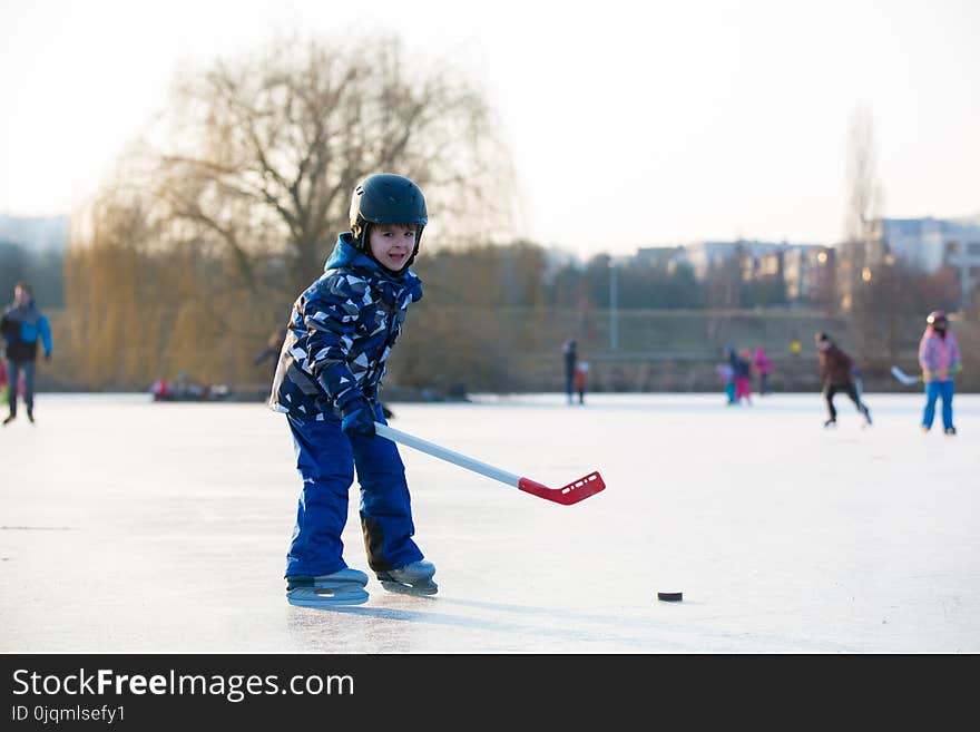 Children, playing hockey and skating in the park on frozen lake, wintertime on sunset