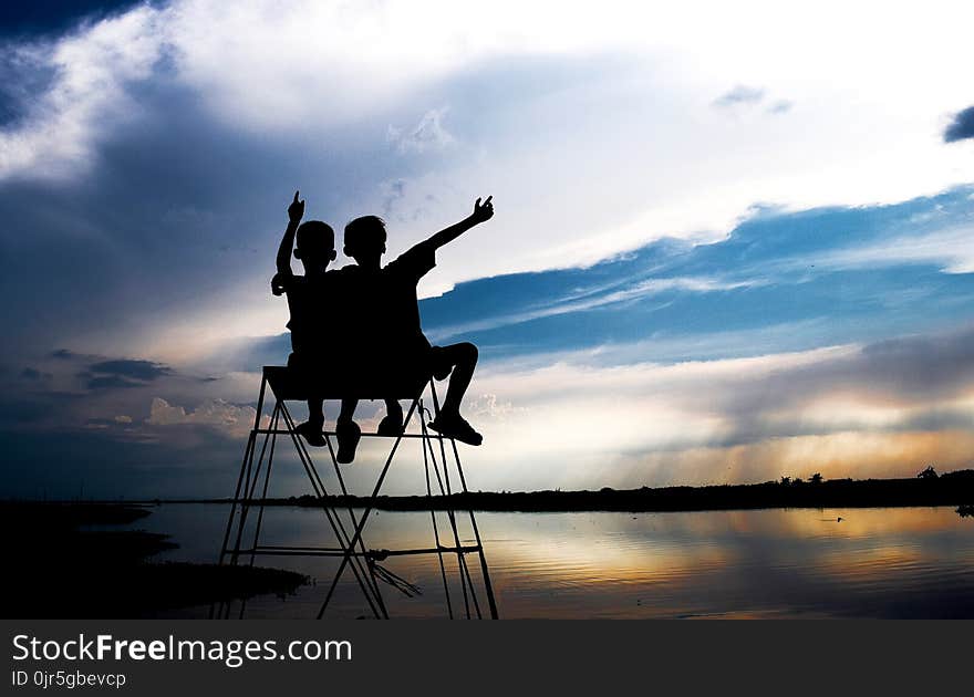 Silhouette of Two Children Looking at Body of Water