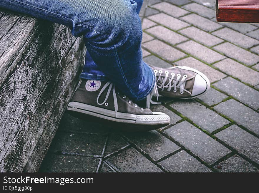 Person Wearing Brown Converse All-star High-top Sneakers and Blue Denim Jeans While Sitting on Bench