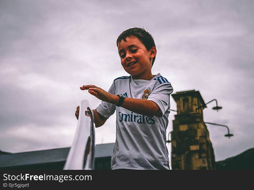 Boy in White and Blue Fly Emirates Jersey Shirt Holding on Stairs Grab Bar Under Gray Skies