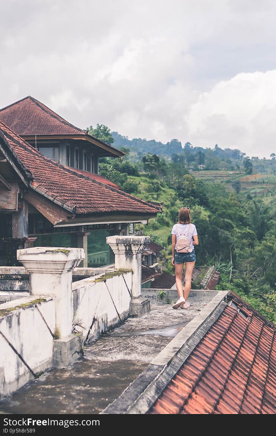 Woman Standing on Gray Concrete Roof Near Mountain Surrounded by Tall Trees