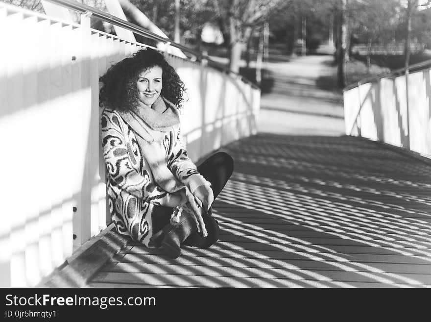 Grayscale Photography of Woman Sitting on Bridge