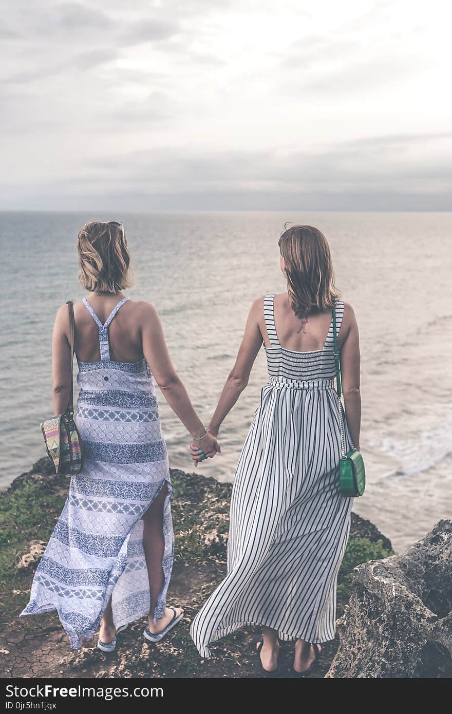 Two Women Wearing Sleeveless Dress Holding Each Others Hand on Cliff