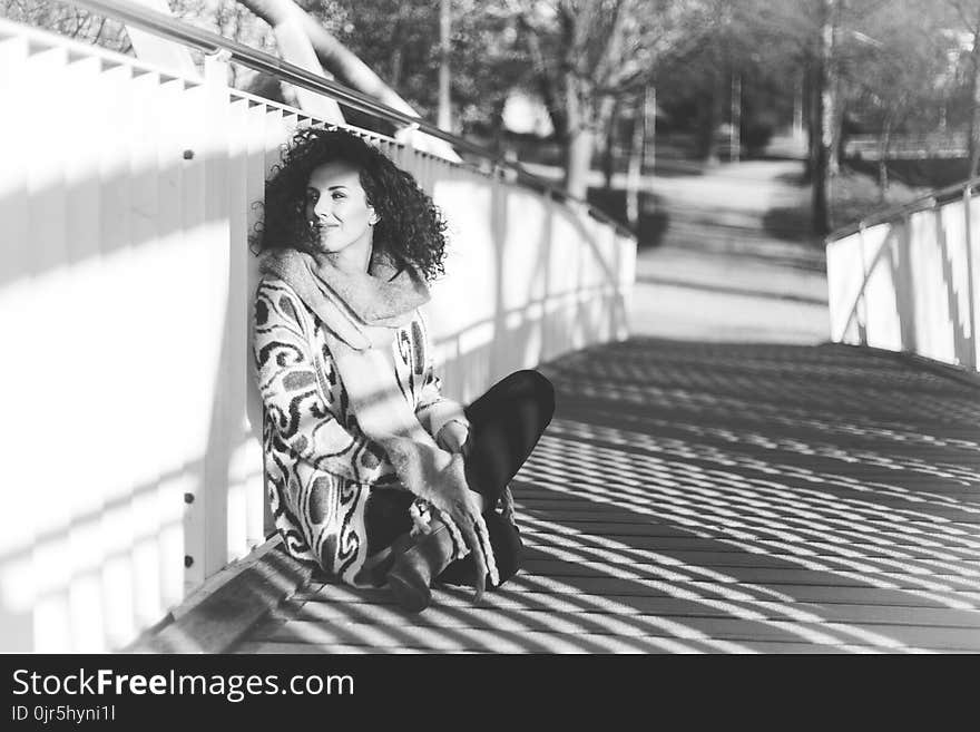 Grayscale Photo of a Woman Sitting Beside a Rail