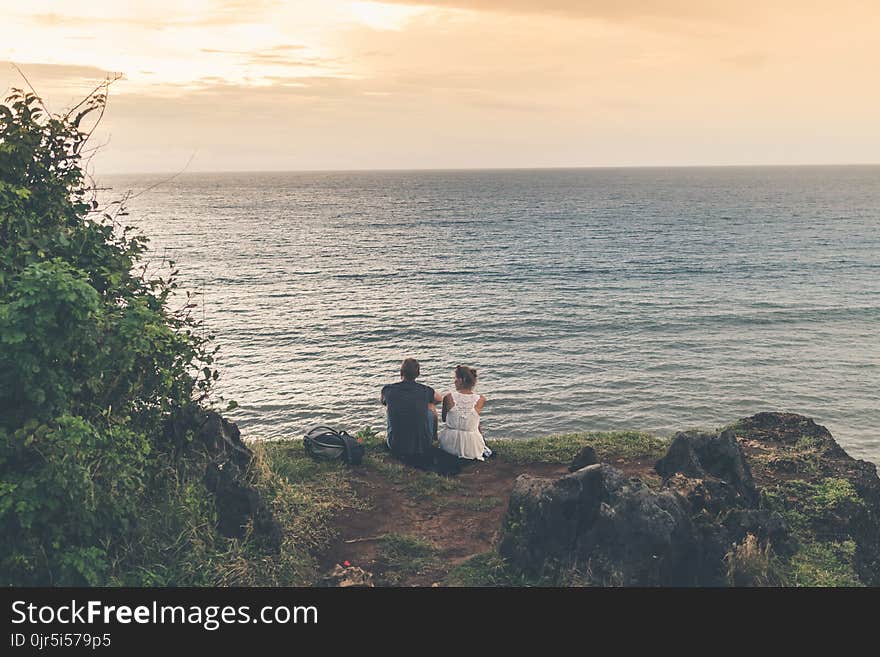 Man and Woman Sitting Near Body of Water