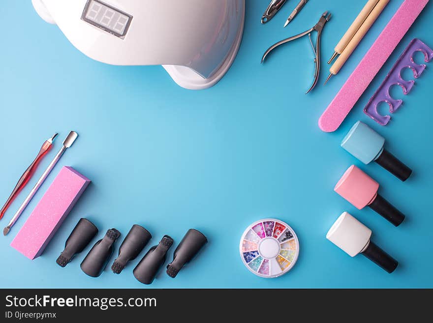 A set of cosmetic tools for manicure and pedicure on a blue background. Gel polishes, nail files and clippers, and the lamp top view